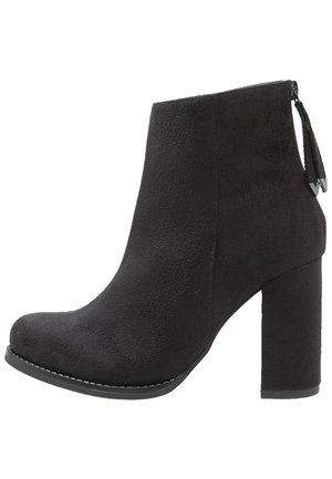 Bottes chelsea noires en daim, à bout rond, avec un talon épais et un détail de zip orné de glands à l'arrière. Texture lisse sans motifs visibles.