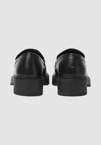 Scarpe in pelle nera con tacco basso a blocco, punta rotonda e dettagli cuciti lungo la suola, viste da dietro.