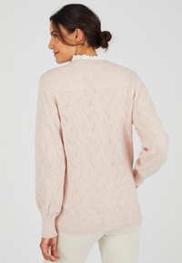 Maglione lavorato a maglia rosa chiaro con motivo a onde testurizzato, polsini e colletto a coste. Maniche lunghe e vestibilità rilassata, design leggermente oversize.