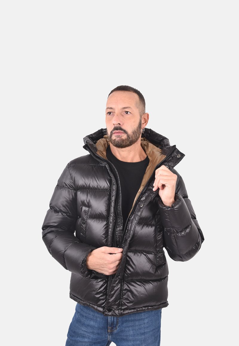 Giacca nera imbottita con cappuccio, dotata di chiusura con zip e polsini elastici. Foderata in tessuto marrone, presenta una texture trapuntata.