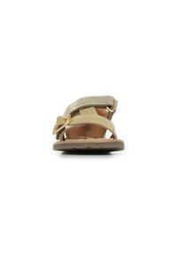 Sandalia beige con una correa plateada brillante y un cierre en la parte trasera. Presenta un diseño de punta abierta, textura suave y una suela marrón resistente.