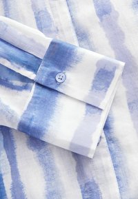 Blå och vit randig skjorta med en mjuk textur, med knappstängning vid ärmen och mjuka, akvarellliknande mönster.