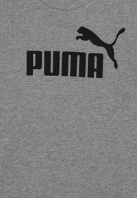 Pelēka kokvilnas T-kreklu ar lielu melnu "PUMA" logotipu un lecošas melnas puma siluetu virs teksta.