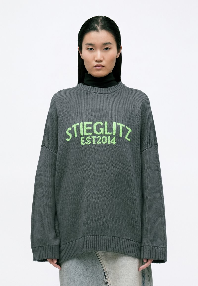 Oversized szary sweter z teksturowanym splotem, prążkowymi mankietami i neonowozielonym napisem "STIEGLITZ EST.2014" na przodzie.
