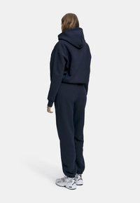 Mørkeblå hettegenser og joggebukse-sett i myk stoff. Hettegenseren har en stor hette og avslappet passform; buksene har elastisk midje og mansjetter.