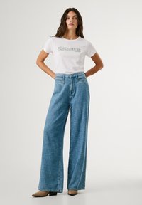 White T-shirt with "PERJEANS" printed in blue, paired with high-waisted, wide-leg blue jeans. Brown pointed heels complete the outfit.