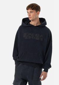 Ναυτικό μπλε oversized φούτερ από βαμβάκι με καγκουρό τσέπη και ανάγλυφο λογότυπο μπροστά. Διαθέτει κουκούλα με κορδόνι και ρίγες στις μανσέτες.