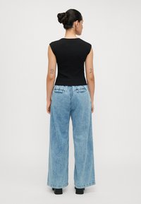 Zwarte, aansluitende mouwloze top gecombineerd met lichtblauwe wijde jeans. De denim heeft een vervaagde wasbeurt en achterzakken met accentstiksels.