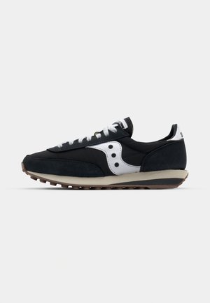 Svart sneaker med et design av semsket skinn og mesh, hvite detaljer, runde perforeringer og en gummisåle med et strukturert mønster.