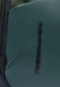 Primo piano di una borsa in pelle verde scuro con logo verticale "Diesel" nero e una cerniera nera testurizzata sul lato.