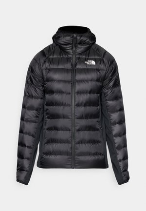 Black puffer jacket with a zip front and hood. Features quilted sections and a logo on the left chest. Stretchy side panels for fit.