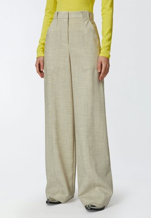 Pantalones beiges de pierna ancha con una tela texturizada, que presentan una cintura alta, bolsillos laterales y pliegues confeccionados; combinados con una blusa de manga larga de color amarillo brillante.