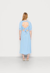 Vestido midi azul com bolinhas, apresentando mangas bufantes, costas abertas com detalhe de laço, e um tecido de textura suave.