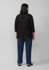 Zwarte gebreide cardigan met driekwartmouwen, geribbelde zoom en een relaxte pasvorm, gecombineerd met blauwe denim, gezien vanaf de achterkant.