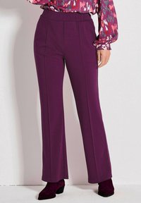 Paarse wijde broek gemaakt van zacht materiaal met een hoge taille en verticale naden, gecombineerd met donkerpaarse enkellaarsjes.