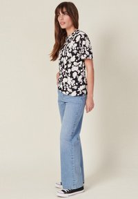 Camiseta negra de manga corta con estampado floral, combinada con jeans acampanados de color azul claro y zapatillas negras. Fondo liso.