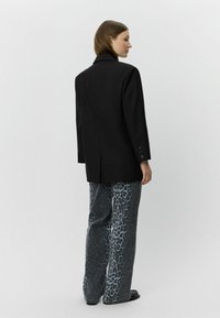 Sacou negru croit, cu guler tăiat, asortat cu pantaloni largi având un model de leopard în nuanțe de albastru și negru.