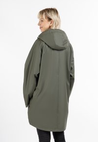 Jachetă impermeabilă de culoare verde măsliniu, cu glugă, croială supradimensionată și textură netedă. Dispune de capse la manșete și un design cu tiv drept.