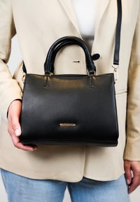 Zwarte leren handtas met een gestructureerd ontwerp, dubbele bovenhandvatten en een verstelbare schouderband. Goudkleurige hardware en logo-detail aan de voorkant.