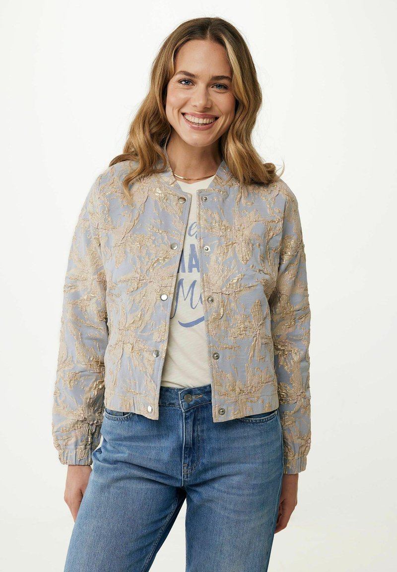 Veste bomber cropped bleu clair avec une broderie dorée texturée, fermetures à pression et poignets côtelés, portée par-dessus un t-shirt graphique blanc.