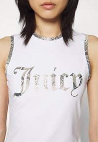 Bílý bezrukávový top s vypouklým vzorem hadího rámu a logem "Juicy" v reflexním hadím potisku. Hladký, přiléhavý design s kulatým výstřihem.