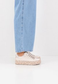 Platform sneakers in beige with a leopard print outsole, featuring a smooth upper, lace-up design, and metallic accents.