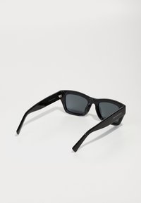 Ochelari de soare negri cu un design pătrată, fabricați din plastic lucios. Lentile întunecate cu brate subțiri ce prezintă detalii de marcă.