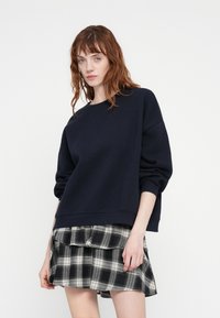 Pull bleu marine en sweat avec un col rond et des épaules tombantes, associé à une jupe à volants en vichy noir et blanc.