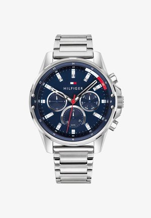 Srebrny metalowy zegarek na rękę z niebieską tarczą, trzema subtarczami pokazującymi 24 godziny, dzień tygodnia i datę, z logo Tommy Hilfiger poniżej godziny 12.