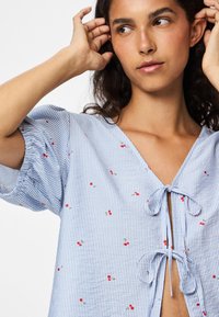 Blue and white striped top with short, puffed sleeves, a deep V-neck, and decorative red cherry embroidery. Features a front tie closure.