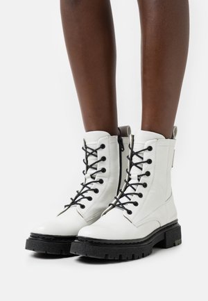 White leather lace-up ankle boots with black laces, chunky black rubber soles, and a side zipper for easy access.