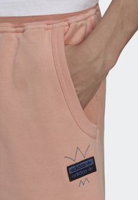 Peach cotton joggers with side pockets, featuring a black and blue Adidas logo patch and ribbed waistband for comfort.