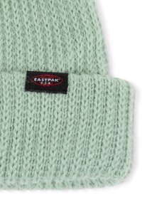 Mintgrön stickad mössa med uppvik och en svart etikett med vit och röd "EASTPAK" märkning.