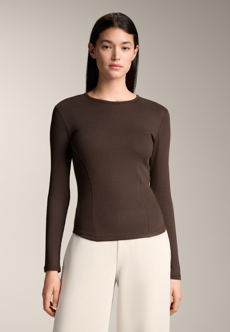 Brown long-sleeve top with a fitted design and ribbed texture, featuring a round neckline and subtle seam detailing. Paired with light-colored pants.