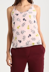 Lichtroze mouwloze top met bloemenprint in zwart, geel en blauw. De stof is lichtgewicht met een gladde textuur en dunne bandjes.