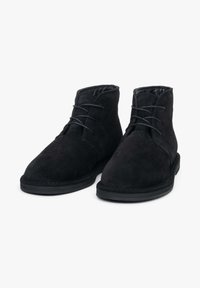 Para czarnych zamszowych botków za kostkę z sznurowadłami i gumową podeszwą, wyeksponowanych na białym tle, widok z przodu.