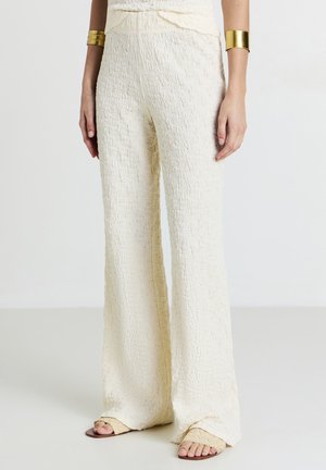 Pantalons larges texturés crème avec une taille ajustée. Le tissu a une apparence froissée et présente une silhouette légèrement évasée.