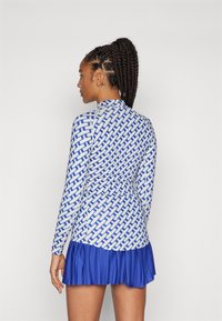 Long-sleeve dress featuring a geometric blue and white pattern, with a pleated blue skirt. Fabric appears smooth with a fitted bodice.