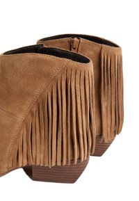 Botines con flecos en piel de ante color marrón claro, con un bajo tacón de madera. El cierre de cremallera y el detalle de superficie texturizada realzan el diseño.