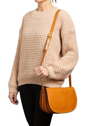 Borsa a tracolla in pelle marrone con pattina curva, tracolla regolabile e dettagli cuciti, abbinata a un maglione beige a texture e pantaloni neri.