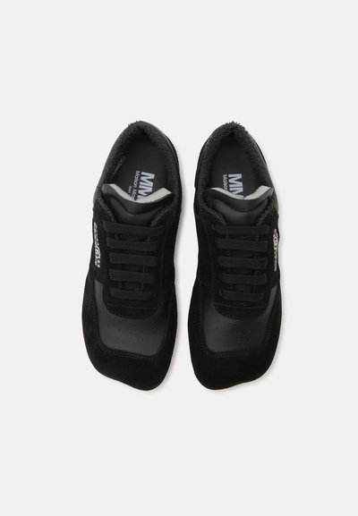 Ζευγάρι μαύρα σουέντ και δερμάτινα sneakers με μαύρα κορδόνια, λευκό λογότυπο στις εσωτερικές σόλες, εμφανιζόμενα από πάνω σε λευκό φόντο.