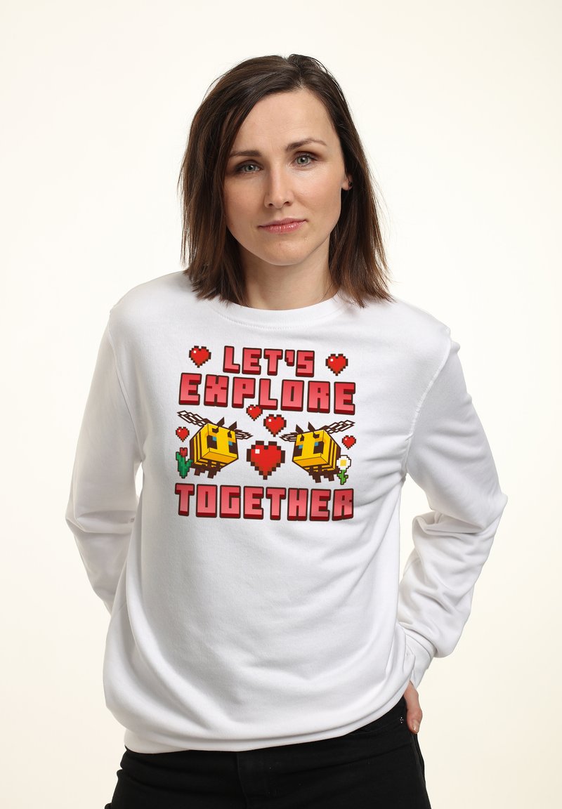 Felpa bianca a maniche lunghe con una grafica di un'ape pixelata colorata, cuori rossi e il testo "ESPLORIAMO INSIEME" in lettere grassetto.