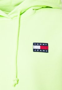 Felpa verde lime realizzata in morbido tessuto, con cappuccio regolabile e un logo rettangolare di Tommy Jeans in nero, bianco e rosso.