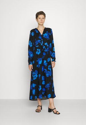 Μάξι φόρεμα σε μαύρο ύφασμα με μπλε floral μοτίβο, μακριά μανίκια, κουμπωτή μπροστινή πλευρά και ζώνη στη μέση. Συνδυάζεται με μαύρες σανδάλια με τετράγωνο τακούνι.