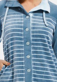 Peignoir rayé bleu et bleu clair en tissu doux, avec un devant à boutons, une capuche et des poches latérales. Des boutons décoratifs améliorent le design.