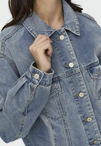 Giacca in denim di colore azzurro chiaro con colletto, chiusura frontale a bottoni e due tasche sul petto. Presenta maniche a sbuffo e cuciture in contrasto.