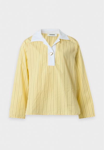 Chemise jaune manches longues avec fines rayures verticales, patte de col blanche et un unique bouton décoratif en forme d'anneau doré au niveau de l'encolure.