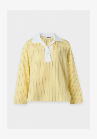 Chemise jaune manches longues avec fines rayures verticales, patte de col blanche et un unique bouton décoratif en forme d'anneau doré au niveau de l'encolure.