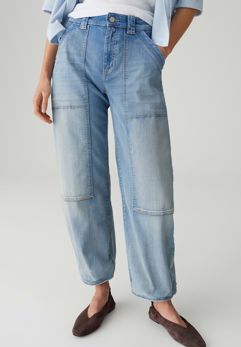 Light blue wide-leg jeans with large patch pockets worn with brown flat shoes and a tucked white top.