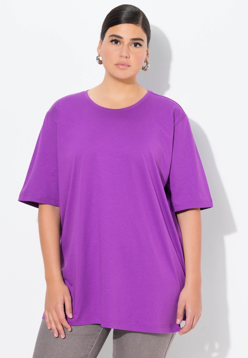 Lila oversized T-Shirt aus weichem Stoff mit kurzen Ärmeln und rundem Ausschnitt, kombiniert mit grauen, schmal geschnittenen Hosen. Einfaches und lockeres Design.